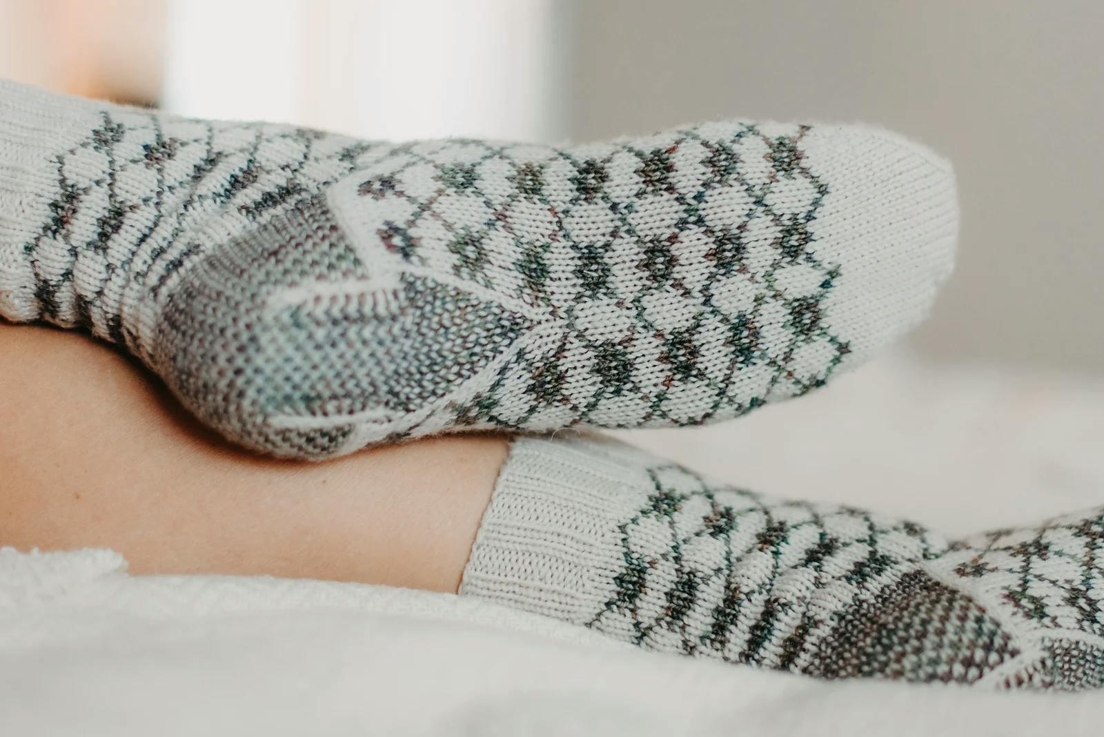 Feet wearing hand-knit cream socks with dark green diamond colourwork patterning