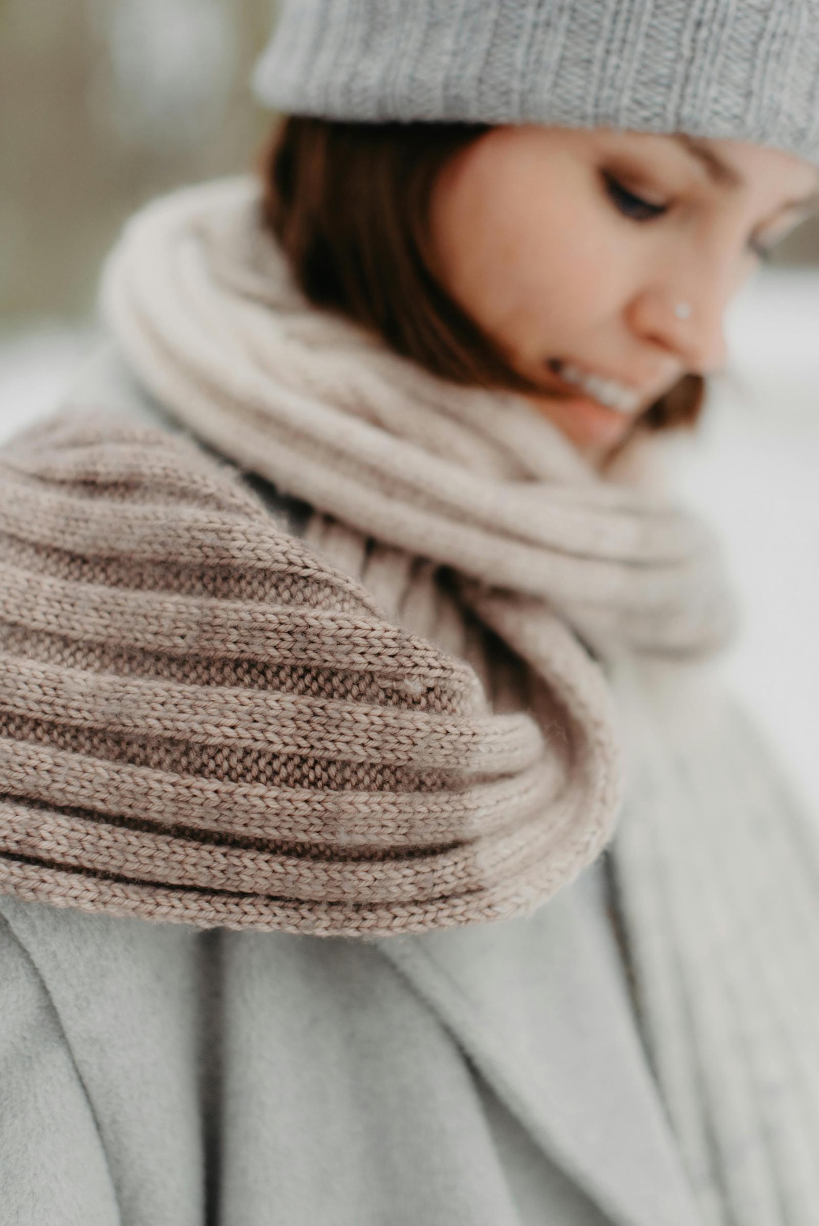 Close-up of the 4x4 Scarf wrapped around the neck in soft neutral striped ribbing, worn with a grey hat and coat