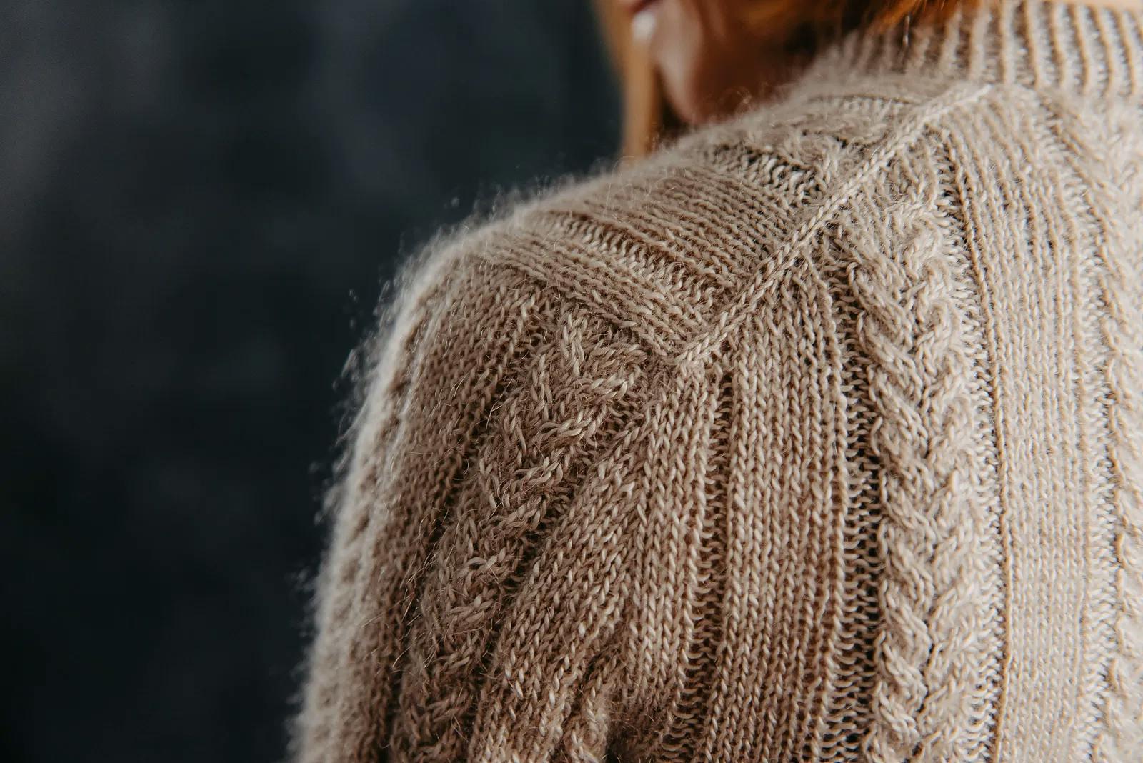 Back view close-up of the Layan Cardigan showing two-by-two cables running across the shoulder and sleeve in sandstorm mohair