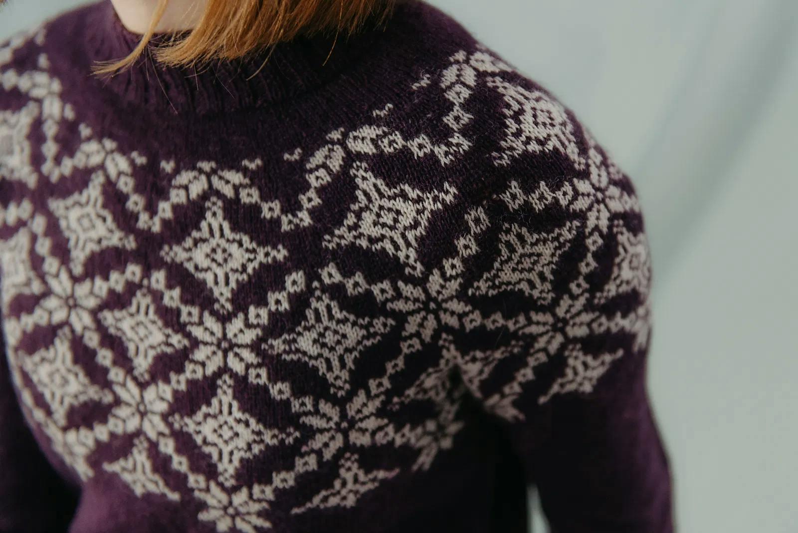 Close-up of the Pasaka Sweater yoke in deep blackberry with cream snowflake colourwork inspired by traditional Latvian mittens