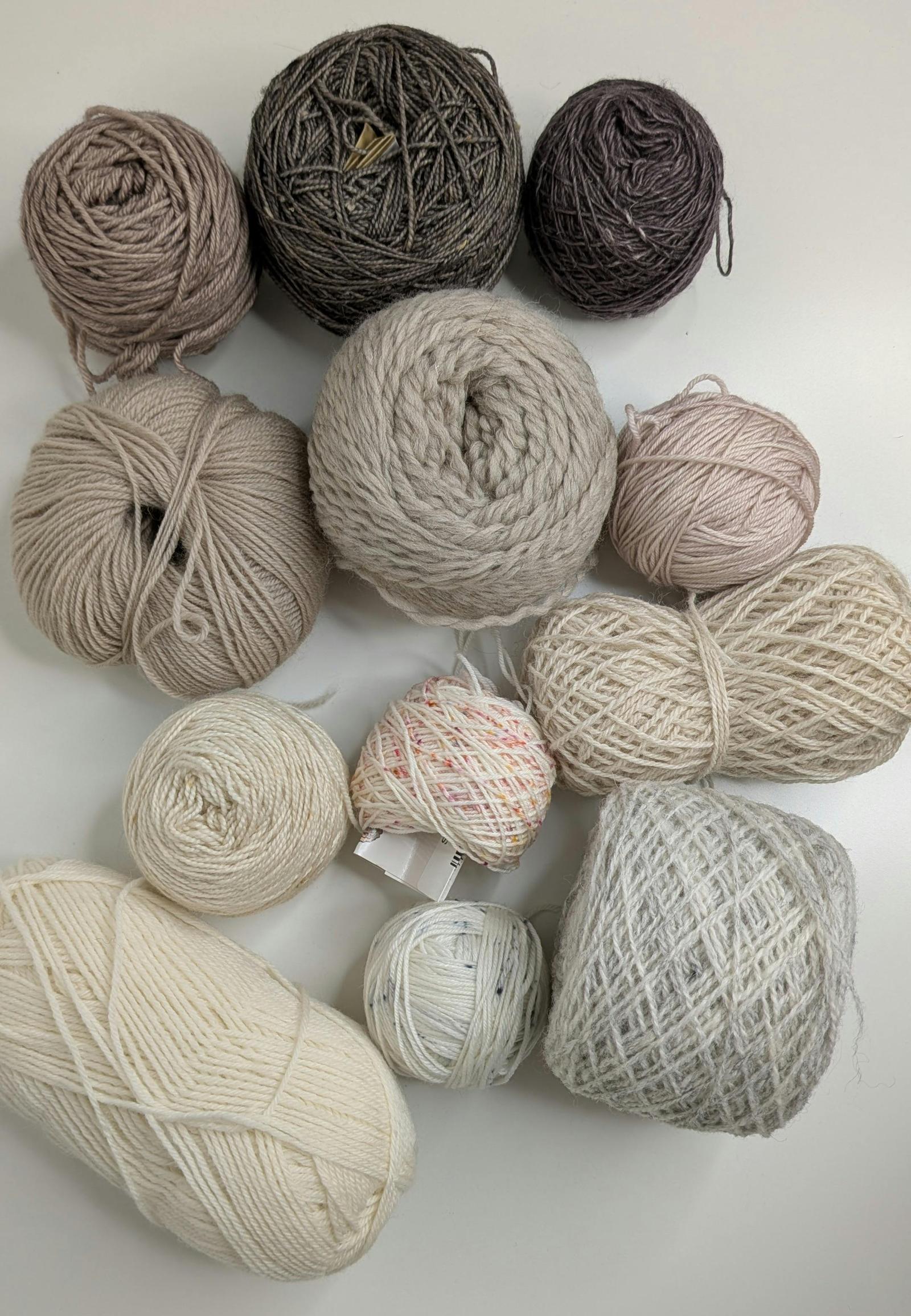 A collection of leftover yarn cakes in neutral shades of cream, beige, grey and dusty pink laid out together